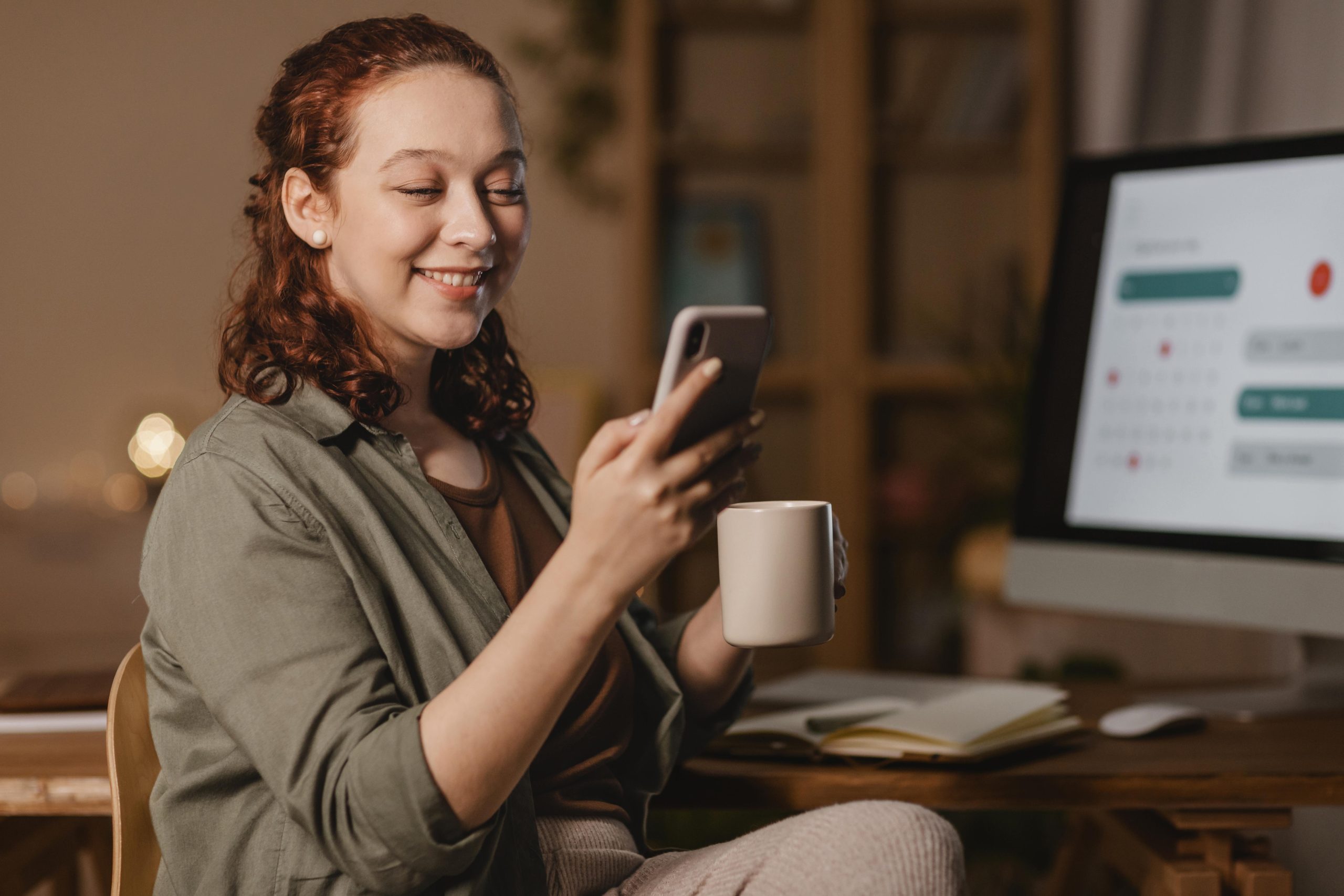 mulher-em-casa-usando-smartphone-na-frente-computador-enquanto-toma-cafe
